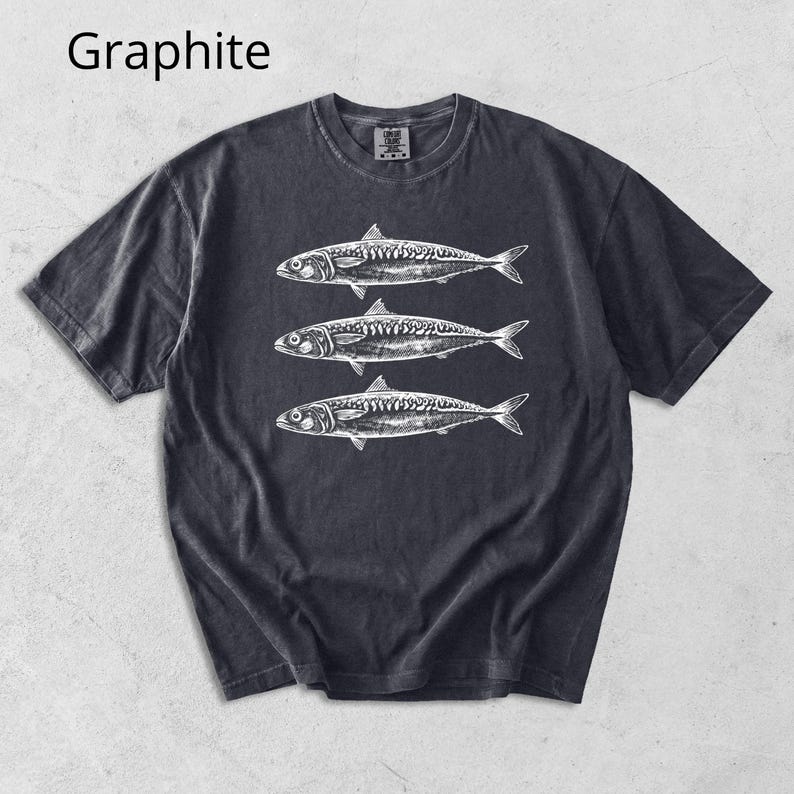 May include: Graphite-colored t-shirt featuring a detailed white illustration of three fish. The design is centered on the front of the shirt. The shirt has a classic crew neck and short sleeves. The word "Graphite" is printed in the upper left corner.