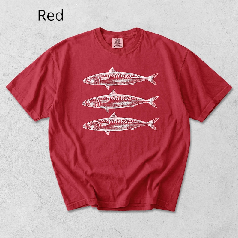 May include: Red t-shirt with a white illustration of three fish. The word "Red" is printed in white in the upper left corner. The shirt is made of a soft material and has short sleeves.
