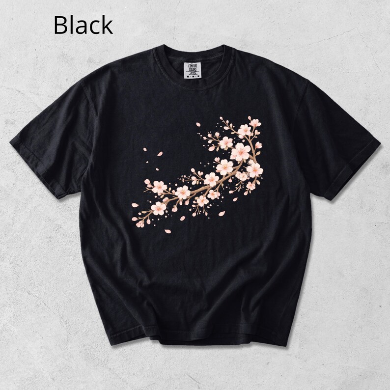 May include: Black t-shirt featuring a floral branch design with pink blossoms and falling petals. The text "Black" is visible in the upper left corner. This short-sleeved tee is a comfortable and stylish addition to any wardrobe.