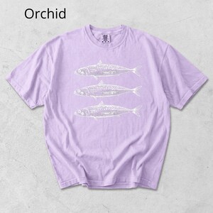 May include: Orchid-colored t-shirt with a crew neck and short sleeves. The shirt features a white graphic of three fish. The word "Orchid" is printed in the upper left corner of the image.