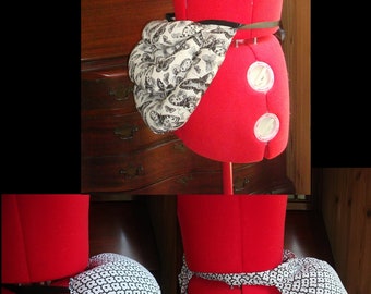 May include: A red dress form with a black belt and a white and black patterned fabric draped over the back. The fabric is gathered and bunched up to create a pouf shape.