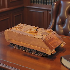 Puede incluir: Un modelo de madera de un tanque militar descansa sobre un escritorio de madera pulida. El tanque está detallado con orugas y torretas. Un libro encuadernado en cuero con un emblema dorado está junto al tanque. El escritorio está en una habitación con paneles de madera y una silla de cuero.