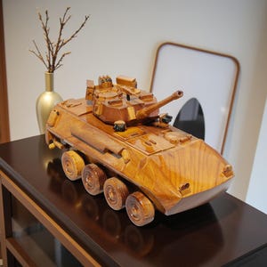 Könnte beinhalten: Detailliertes Holzmodell eines Militärpanzers, das aufwendige Handwerkskunst zeigt. Der Panzer verfügt über einen drehbaren Turm, mehrere Räder und eine natürliche Holzmaserung. Das Modell wird auf einer dunkelbraunen Oberfläche präsentiert.