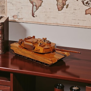 Puede incluir: Maqueta de madera de un tanque militar, con un cañón largo y detalles intrincados en las orugas. El tanque está hecho de madera marrón claro y se encuentra sobre una superficie marrón oscuro, con un mapa del mundo de fondo.