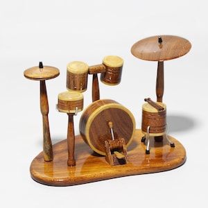May include: A miniature wooden drum set with a glossy finish. The set includes a bass drum, snare drum, cymbals, and a high hat, all mounted on a wooden base. The drum set is made of wood and has a natural wood color.