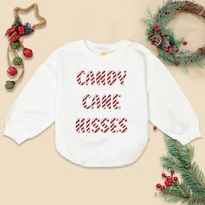 May include: White sweatshirt with the words "CANDY CANE KISSES" in red and white candy cane stripes. The sweatshirt is a crew neck style. Christmas-themed apparel.
