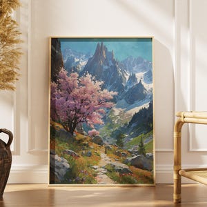 May include: A framed landscape art print featuring a mountain scene with a path, a pink flowering tree, and snow-capped peaks. The artwork has a gold frame and is displayed indoors, leaning against a white wall.