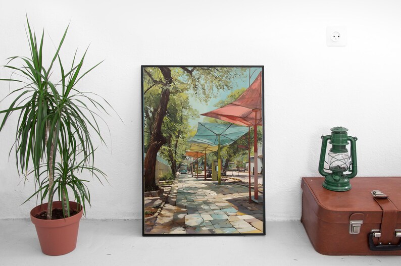 Puede incluir: Impresi&oacute;n art&iacute;stica enmarcada que representa un camino empedrado soleado bordeado de sombrillas de colores. La pintura presenta una paleta vibrante de verdes, azules y rojos, creando una escena exterior serena. La obra est&aacute; enmarcada en negro.