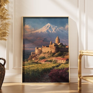 Puede incluir: Una pintura de paisaje enmarcada representa una montaña con una cima nevada y una fortaleza en una ladera. La obra de arte presenta una paleta de colores cálidos con tonos de marrón, verde y azul. La pintura se exhibe en una pared blanca.