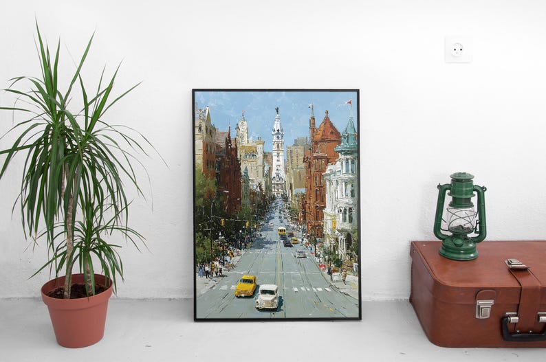 May include: An oil painting of a city street scene with buildings on either side and a tall white tower in the distance. The painting has a black frame and is displayed on a white wall. Two yellow cars and one white car are on the street.