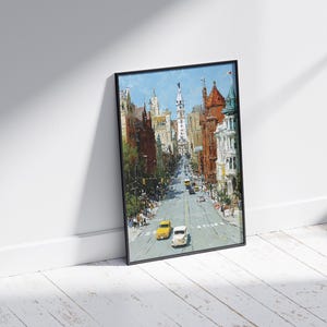 May include: A framed art print depicting a city street scene. The painting features a perspective view of a street lined with buildings in shades of brown, red, and white. Yellow and white cars are on the road. The sky is blue.