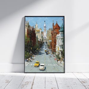 May include: An oil painting print of a city street scene, framed in black. The artwork depicts a wide avenue lined with buildings in shades of brown, red, and white. Two vintage cars, one yellow and one white, are in the foreground.