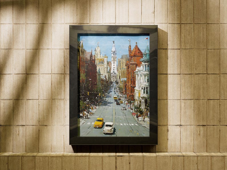 May include: A framed cityscape painting depicting a wide street lined with buildings in various architectural styles. The artwork features a blue sky and several cars, including yellow and white vehicles, on the road. The frame is black.