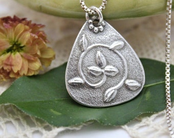 May include: A silver pendant necklace with a detailed design of a stylized leaf and vine. The pendant is teardrop shaped and has a textured surface.