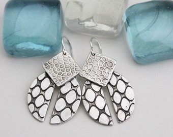 May include: A pair of silver earrings with a geometric design. The earrings are made of two pieces, a square and a half-circle, both with a textured surface.