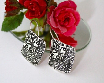 May include: Silver dangle earrings with a square-shaped design featuring intricate black filigree patterns.