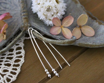 May include: A pair of silver dangle earrings with three small silver beads on each earring.