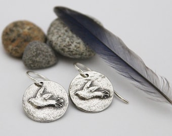 May include: A pair of silver earrings with a textured finish. Each earring features a small, raised image of a bird in flight.