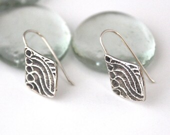 May include: A pair of silver earrings with a geometric design. The earrings are made of textured metal and have a diamond shape.