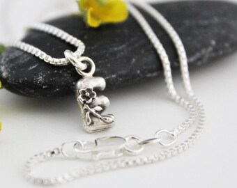 May include: A silver chain necklace with a small silver charm in the shape of the letter E. The charm has a delicate floral design.