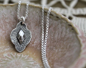 May include: A silver necklace with a pendant featuring a geometric design and a textured leaf shape.