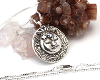 May include: A silver necklace with a round pendant featuring a stylized face of the sun with closed eyes and a starburst design. The pendant is surrounded by a detailed mandala pattern.
