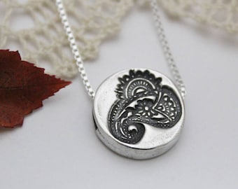 May include: A silver necklace with a round pendant featuring a black paisley design.