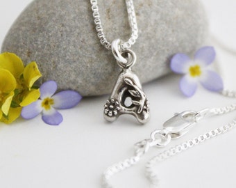 May include: A silver necklace with a delicate chain and a charm in the shape of the letter A. The charm is decorated with small flowers and leaves.