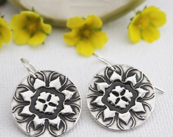 May include: A pair of silver earrings with a black and white mandala design. The earrings are oval shaped and have a hook closure.