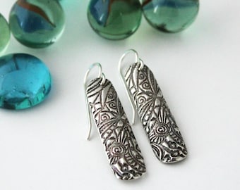 May include: A pair of silver dangle earrings with a detailed, intricate pattern. The earrings are silver and have a long, rectangular shape.