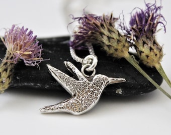 May include: A silver hummingbird pendant necklace with an intricate, detailed design. The pendant is hanging from a silver chain.