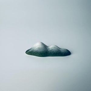May include: A cloud-shaped ornament with a colour gradient. The base is dark green, fading to lighter green and then white at the top. The object has a smooth, rounded shape, resembling a small cloud.