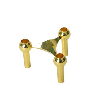Könnte beinhalten: Ein goldfarbener Kerzenhalter mit drei Beinen. Die dreieckige Basis trägt drei zylindrische Beine, die jeweils mit einer kugelförmigen Tasse für Kerzen versehen sind. Das Design ist schlicht und elegant, passend für verschiedene Einrichtungsstile.