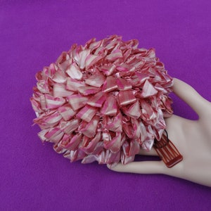 May include: A pink and white striped ribbon hair bow with a brown comb attached. The bow is made of many small loops of ribbon and is shaped like a ball.