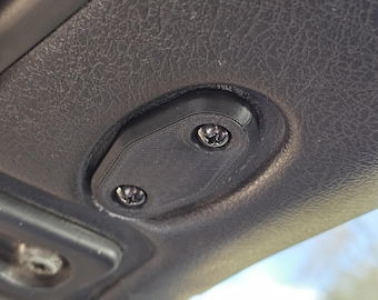 May include: A close-up of a black, 3D-printed cover with two screws. The cover is oval-shaped and has a textured surface. The screws are silver and are partially visible.