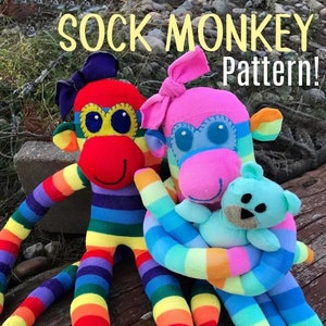 May include: Two sock monkey toys, one red and rainbow striped and one pink and rainbow striped, sitting on a wooden surface. The pink monkey is holding a small blue teddy bear. The text "SOCK MONKEY Pattern!" is at the top of the image. The text "suzyssiitcom.com" is at the bottom of the image.