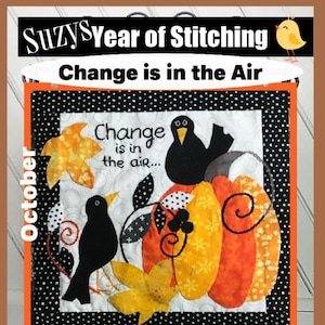 Può includere: Un arazzo trapuntato con un bordo a pois bianchi e neri. Il design presenta una zucca, uccelli neri e foglie autunnali. Il testo "Change is in the air..." è incluso. La parola "October" è sul lato sinistro. La parte superiore recita "Suzy's Year of Stitching".