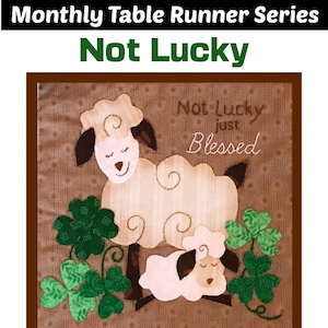 Puede incluir: Un camino de mesa marrón y verde con un diseño acolchado que presenta dos ovejas blancas y tréboles. El texto "Not Lucky Just Blessed" está bordado en el camino de mesa.