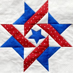 May include: A square quilt block featuring a central blue star, surrounded by red polka-dot and blue fabric shapes on a white background. The design is a geometric star pattern, perfect for patriotic-themed crafts.