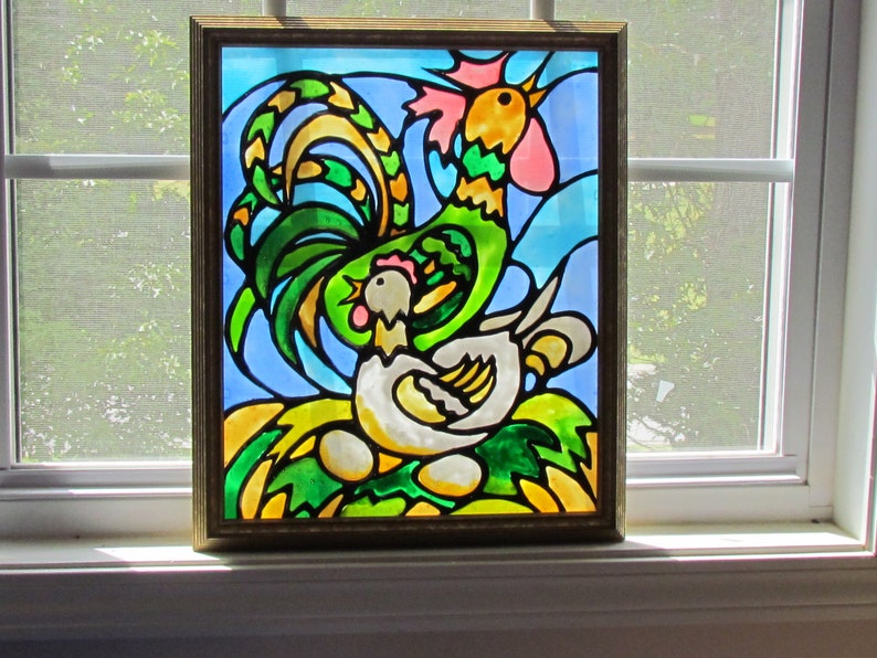 May include: A stained glass window depicting a rooster and a hen. The rooster is green, yellow, and pink, with a large, elaborate tail. The hen is white with a pink comb. The background is blue and green.