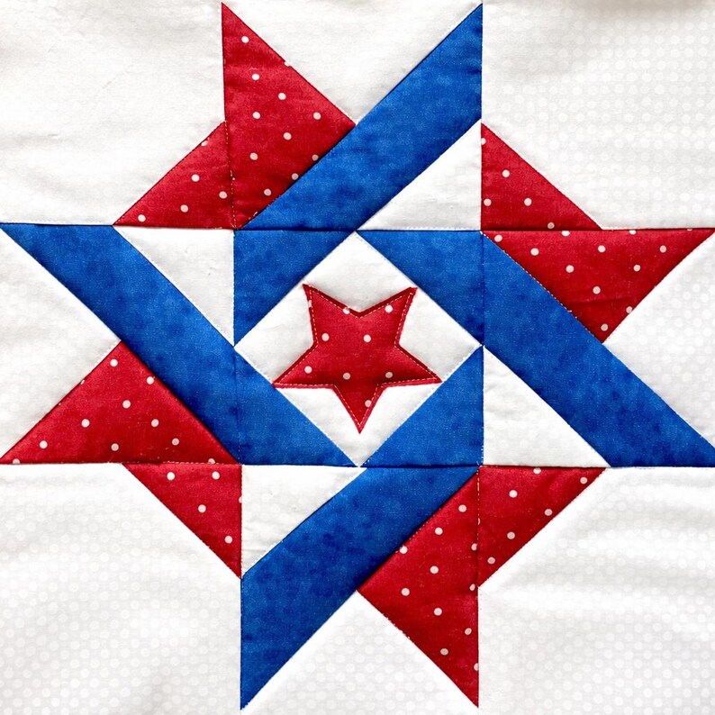 May include: A square quilt block featuring a star design in red, white, and blue. The central star is red with white polka dots, surrounded by blue and red geometric shapes on a white background. The design is reminiscent of patriotic themes.