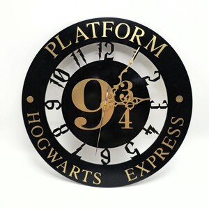 May include: A black and gold circular wall clock with the words "PLATFORM" and "HOGWARTS EXPRESS" around the edge. The clock face features the number "9 3/4" in gold, with gold clock hands. The clock is a decorative item.