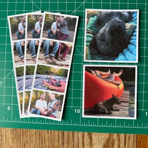 May include: A selection of printed photographs. One strip of photos shows two people in outdoor settings. Two individual photos feature a black dog and a dog on a dock near a red canoe. The photos are on a green cutting mat.