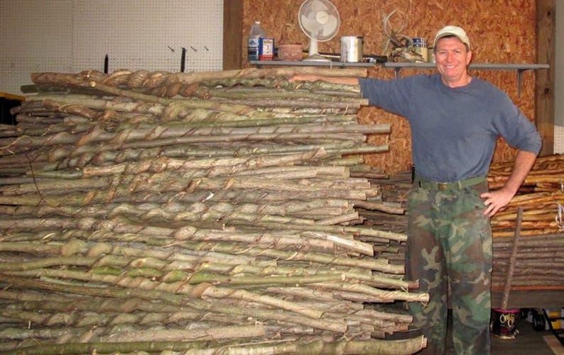 May include: A large stack of natural wooden walking sticks and staffs, many featuring a distinct spiral or twisted vine pattern along the length of the bark. The sticks are arranged horizontally in a pile, showcasing various thicknesses and textures.