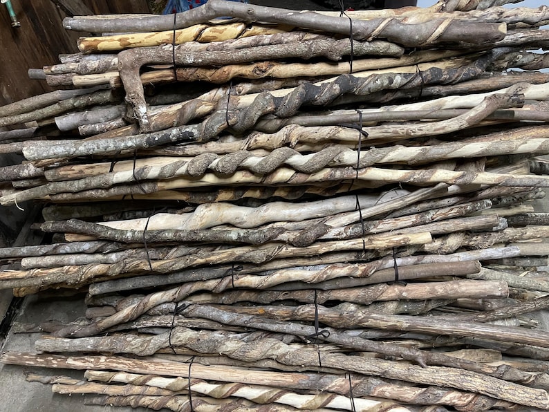 May include: A large collection of natural wooden walking sticks stacked horizontally and secured with black ties. Each stick features a unique, twisted spiral pattern carved into the bark, showcasing varying shades of brown, tan, and grey wood.