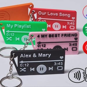 Puede incluir: Una colección de llaveros coloridos en naranja, verde, rojo, rosa y negro, cada uno diseñado para parecerse a una interfaz de reproductor de música. Los llaveros presentan texto como "My Playlist" y "Our Love Song", junto con controles de reproducción/pausa e indicadores de tiempo.