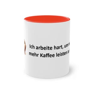 Könnte beinhalten: Weißer Keramikbecher mit roter Innenseite. Der Becher trägt den deutschen Text "Ich arbeite hart, um mehr Kaffee leisten zu" in Schwarz, was übersetzt "Ich arbeite hart, um mir mehr Kaffee leisten zu können" bedeutet.