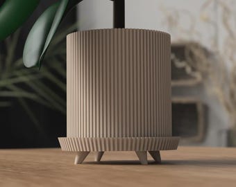 May include: A beige cylindrical planter with vertical grooves. It has a matching base supported by three small, white, conical legs. The design is modern and minimalist, suitable for indoor plants. The planter is approximately 15 cm in height.