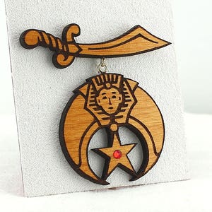 May include: A wooden pendant featuring a crescent moon and a five-pointed star with a red jewel in the center. The pendant is attached to a wooden scimitar.