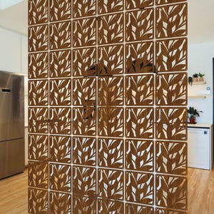 May include: A decorative room divider made of square panels with a leaf design. The panels are a warm brown color and create a semi-transparent screen. The divider is in a modern kitchen setting.
